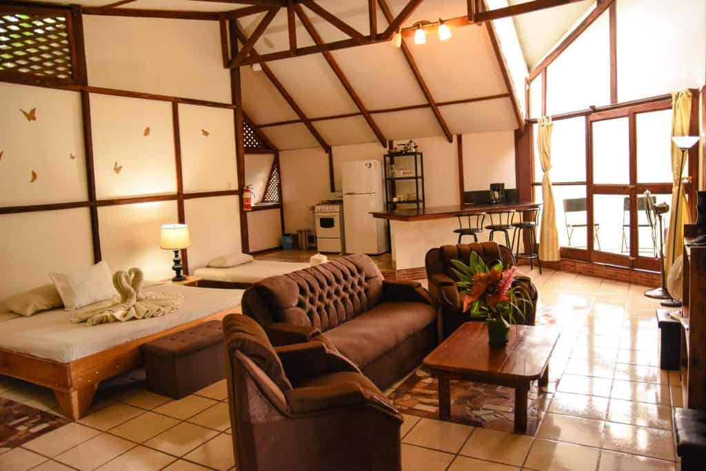 Image of Family Suite room, showing two beds, brown sofa and chairs, breakfast bar and kitchen beyond. Roof is sloped with wooden beams