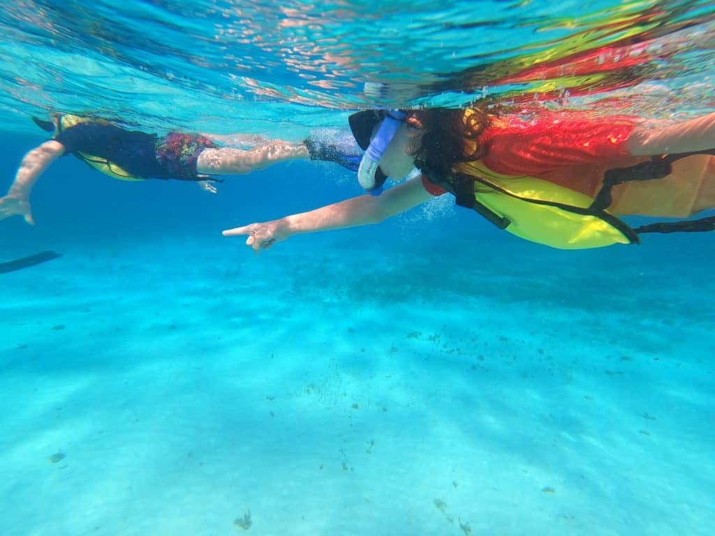 Boy snorkelling in azure clear sea, pointing to giant starfish on the seabed