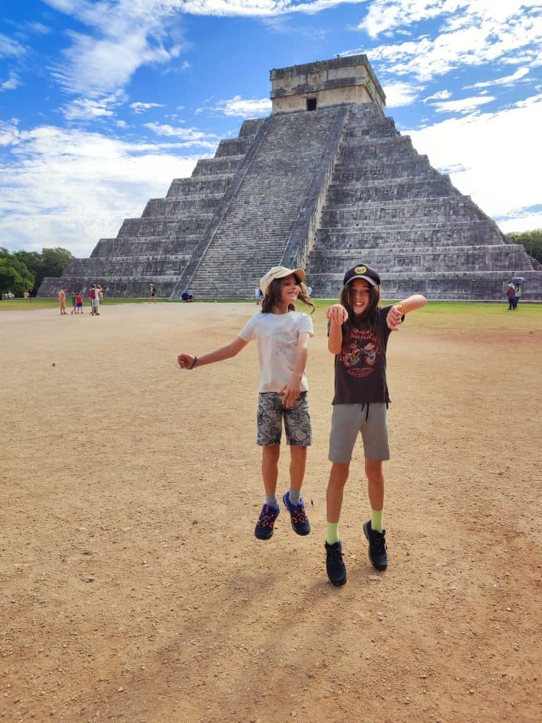Two boys jump in the air in front of El Castillo pyramid at Chichen Itza