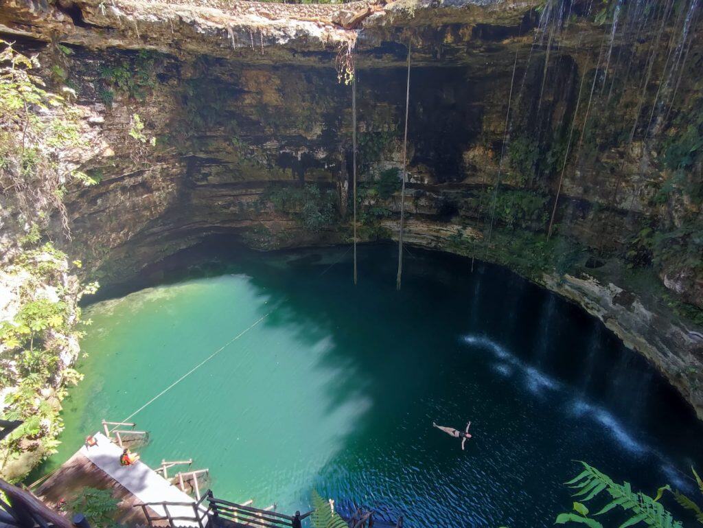 WOman drifts on her back in the middle of an underground cenote. The water is a green blue colour and the wall are sheer drops of rock
