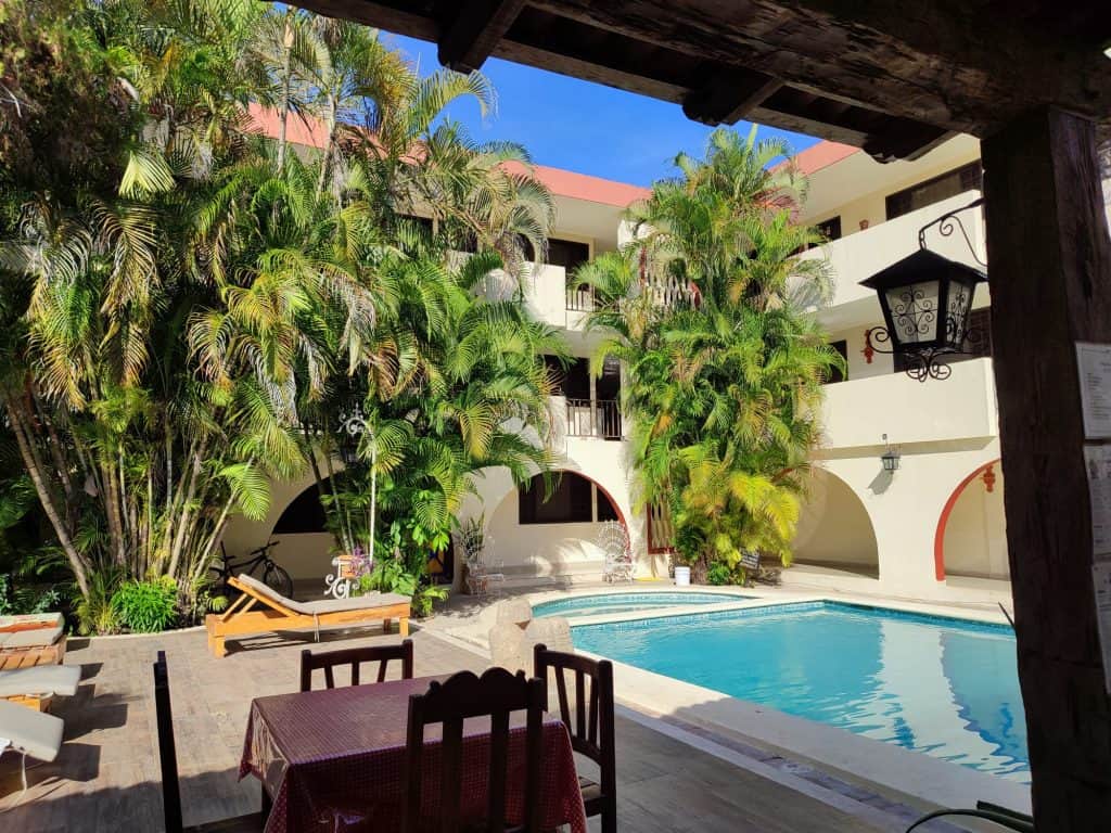 Courtyard with pool to the left in small hotel. There are sunloungers by the pool and tall palm trees around the edge of the courtyard
