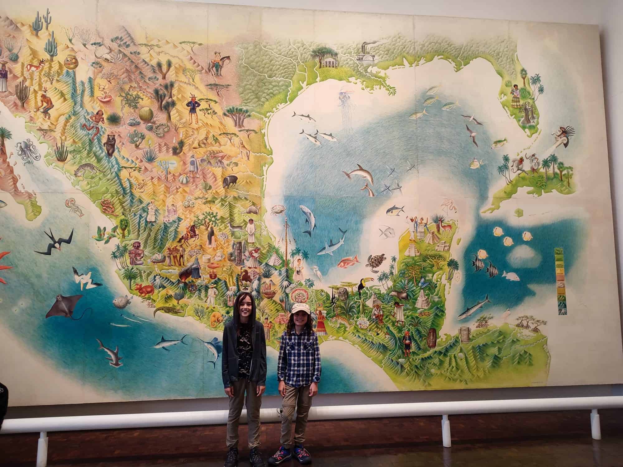 Two boys stand in front of a giant illustrated map of Mexico
