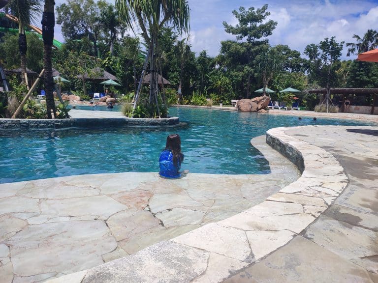 Young boy sits on the edge of a lagoon style swimming pool at Waterbom waterpark in Bali