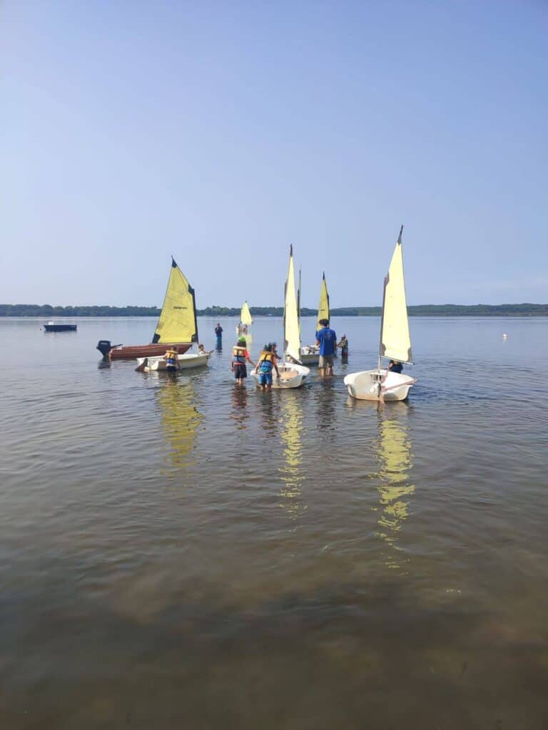 Group of children push small sailboats out on to a lake at Le Col Vert campsite in France