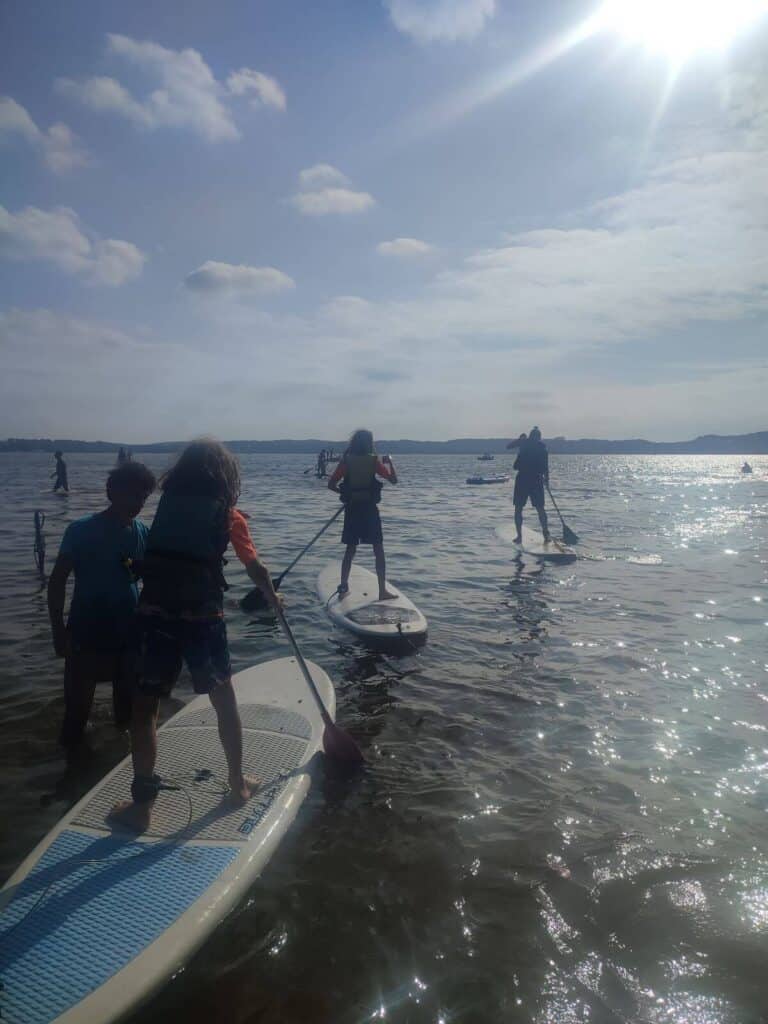 Family paddleboards on a sun drenched lake at Le Col Vert campsite in France.