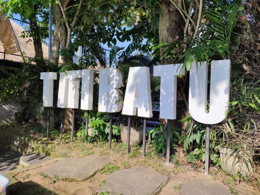 The large Titi Batu sign surrounded by lush greenery and trees, capturing the tropical ambiance at Titi Batu Ubud.