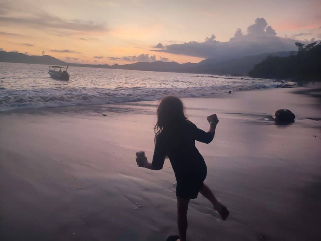 A silhouette of a child balancing on one leg on a beach at sunset on a boat tour to see the bioluminescence in Costa Rica.