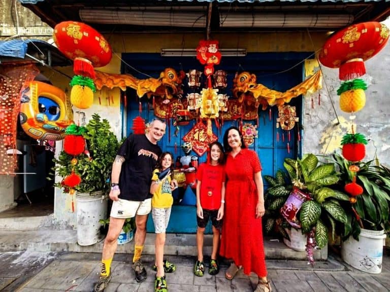 Family of four - man, woman and two young boys - stand in front of a doorway in Penang, Malaysia that is decorated with Chinese lanterns for Chinese New Year,
