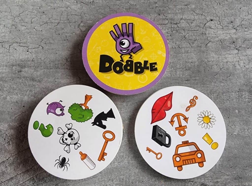 Dobble game tin and a selection of cards sit on a table. One of our top family travel game picks!