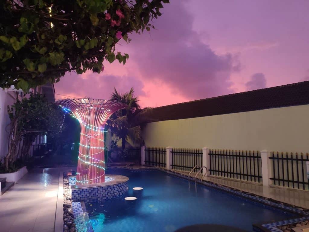 The swimming pool at Duong Dong Hotel in Phu Quoc, Vietnam at night. The sky is a deep pink sunset.