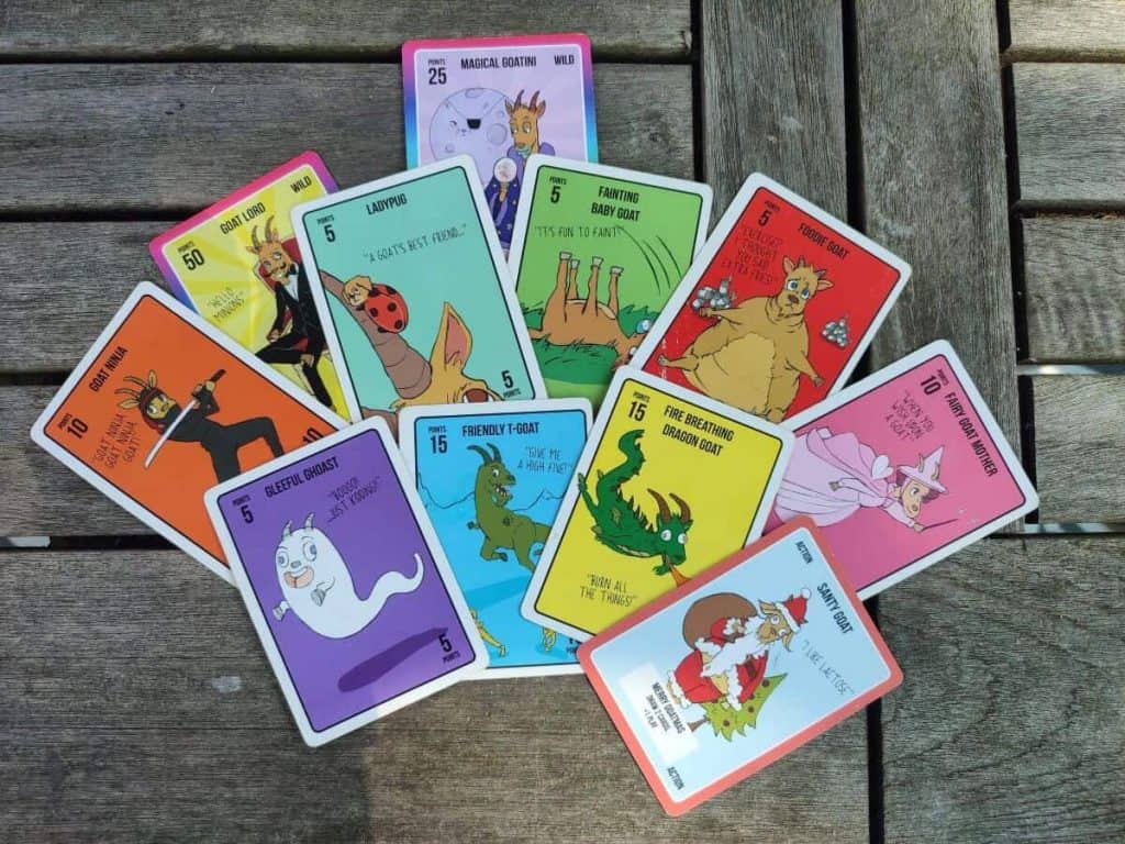 A selection of colourful cards from the game Goat Loads laid out on a wooden table.