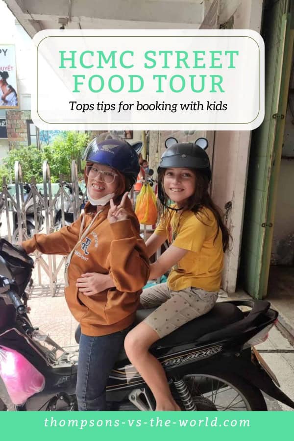 Lively street scene in Ho Chi Minh City (HCMC) featuring two people wearing helmets and riding on a motorbike, with a backdrop of parked scooters and urban surroundings. Text overlay reads "HCMC STREET FOOD TOUR - Top tips for booking with kids" in green and white. Perfect for families planning a street food tour in HCMC with kids! Save this pin to your Pinterest board for later reference.