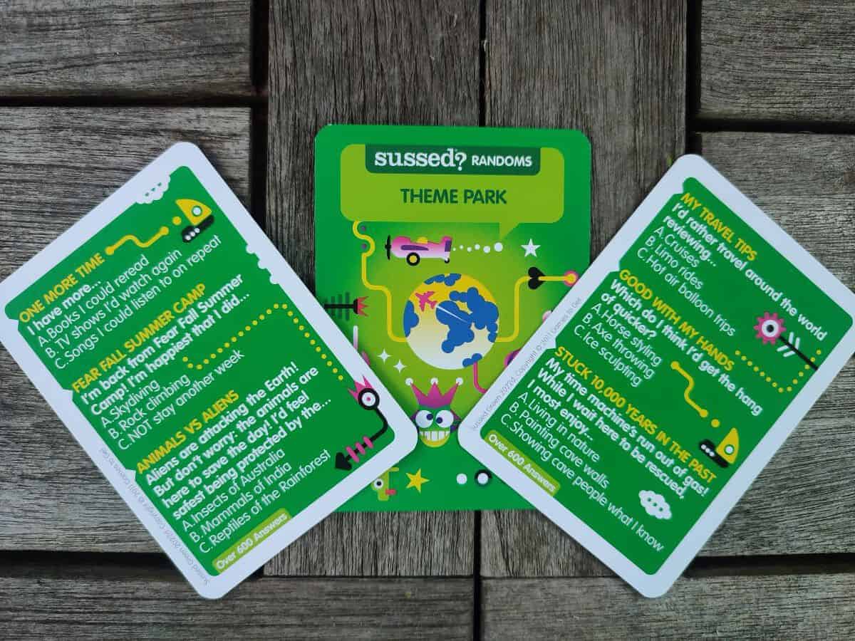Three green Sussed cards laid out on a wooden table. Each has three questions listed for the player on various themes.