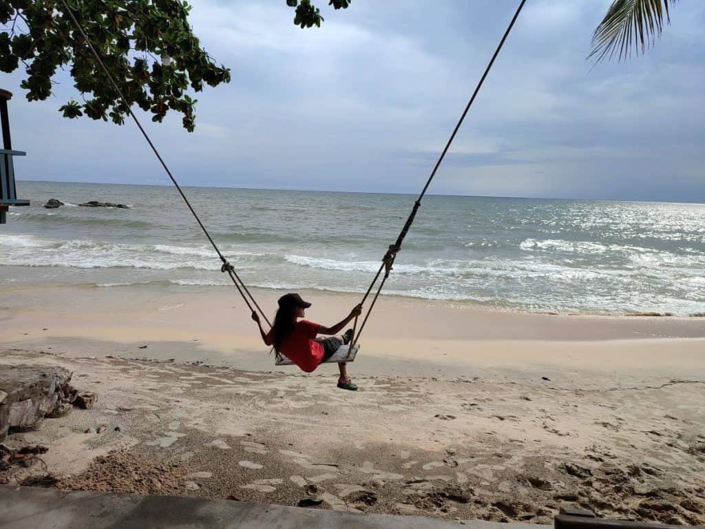 Boy swings out on a wooden swing across the beach in Phu Quoc, Vietnam