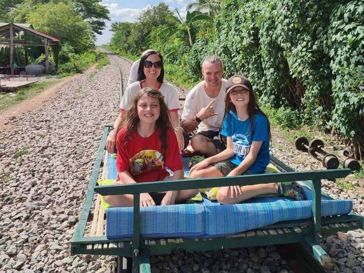 Family of four sit cross-legged on a small cart-lie carriage made from bamboo on the tracks of the Bamboo train in Battambang, Cambodia.