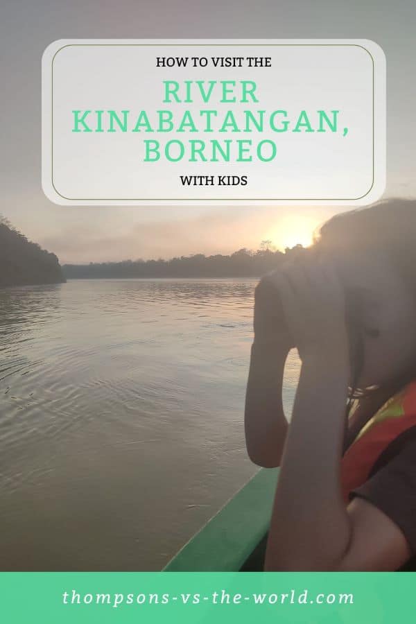 Boy in an orange lifejacket with binoculars looks out from a boat on the Kinabatangan River at sunrise. The text overlay reads 'A Guide to visiting the River Kinabatangan, Borneo with Kids' - pin this image now for your planning later.