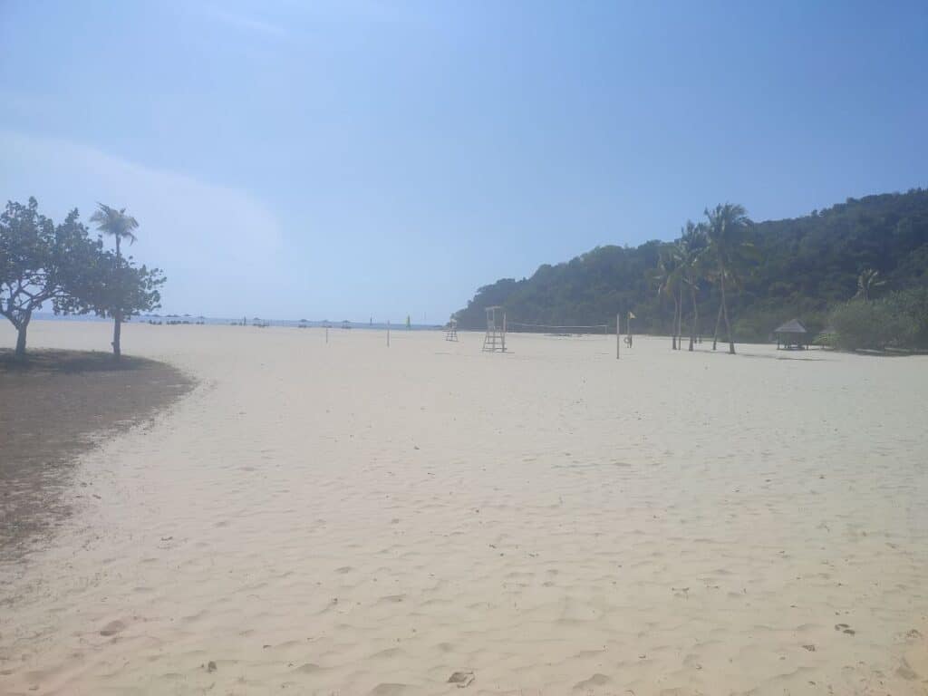 Wide sandy beach with palm trees, lifeguard chairs, and calm sea views at Shangri-La Rasa Ria in Borneo under a clear blue sky. This peaceful scene reflects the spacious beachfront setting discussed in a Shangri-La Rasa Ria review for families seeking a relaxed tropical escape.