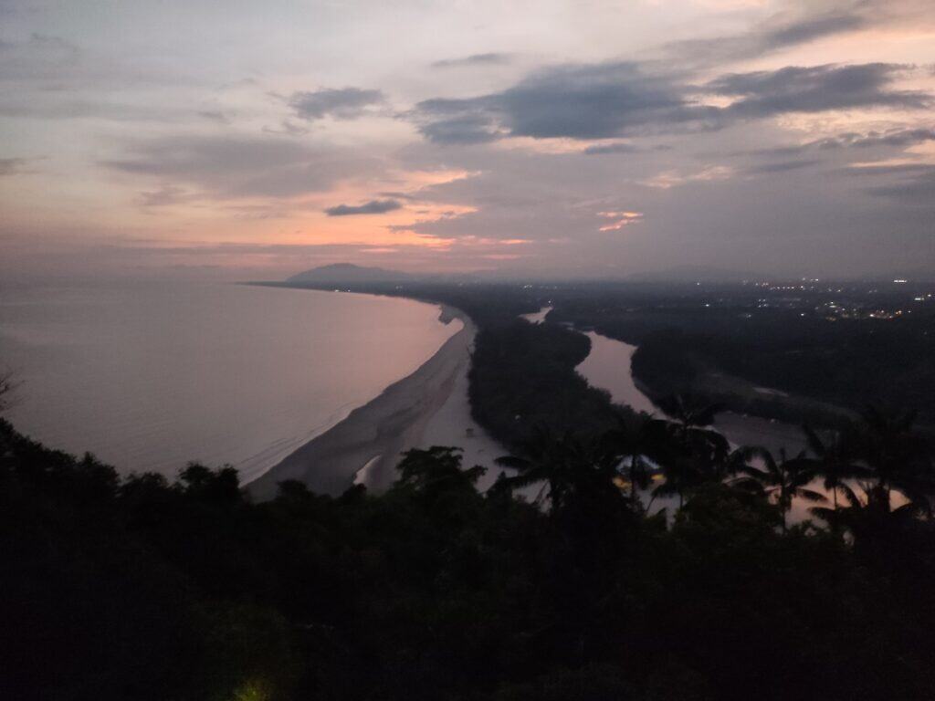 Sunset view overlooking the coastline, river inlet, and surrounding rainforest near Shangri-La Rasa Ria in Borneo with soft pink and orange skies. This scenic outlook captures the natural beauty of the area, showcasing the resort’s unique blend of beach and jungle landscapes described in this Shangri-La Rasa Ria Review..