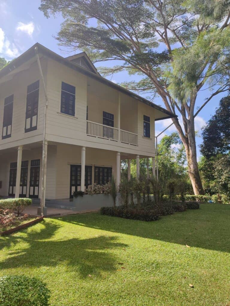 A white clapboard, two storey house with wrap-around verandas on the ground and top floor stands in manicured green lawns in Sandakan, Borneo. This was the home of the famous novelist Agnes Keith during her time in Borneo.