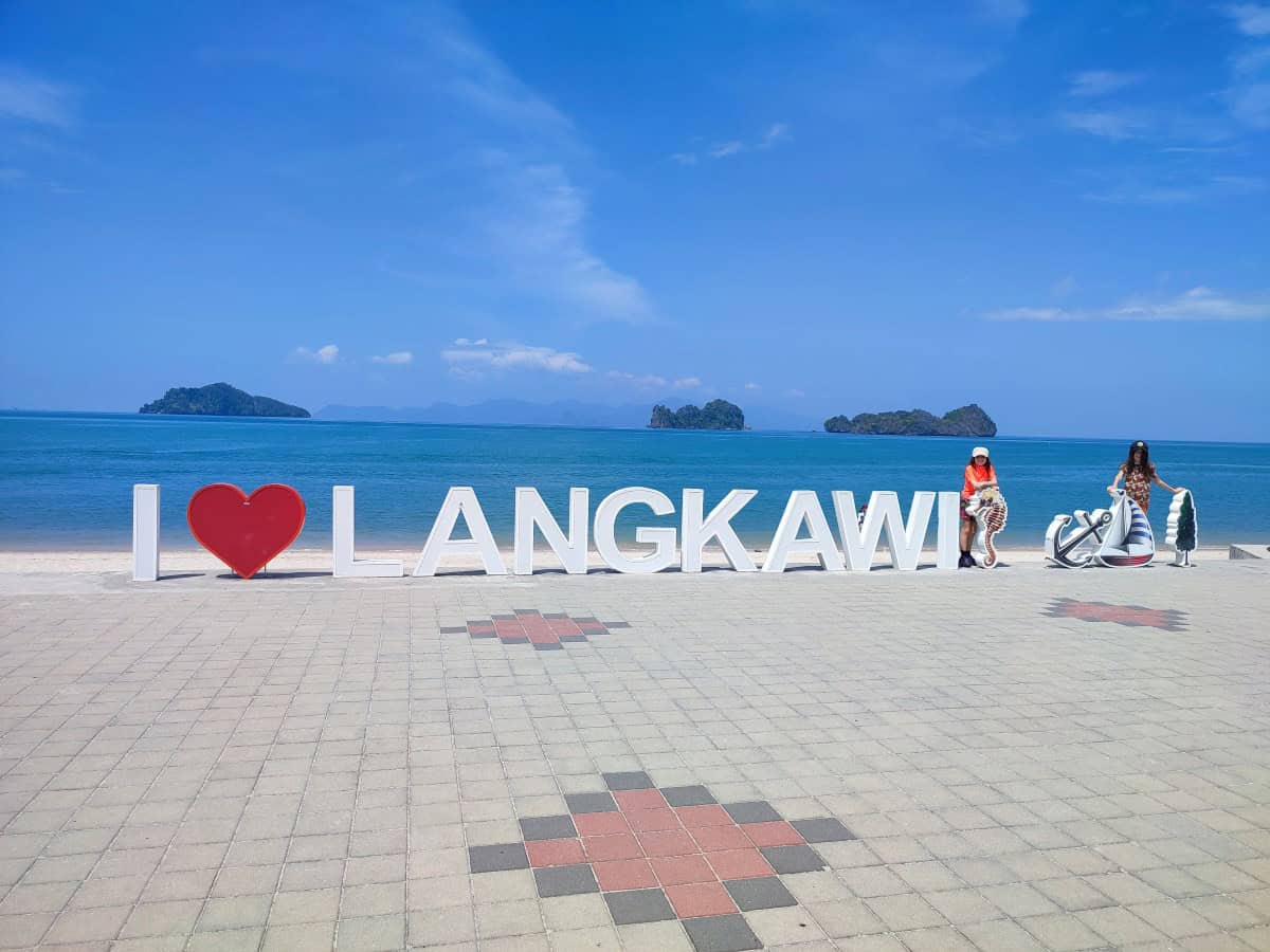Large I love Langkawi sign along the waterfront with blue sea and small green islands in the background under a bright sky. This iconic seaside landmark is a must visit stop on a Langkawi Itinerary for families.