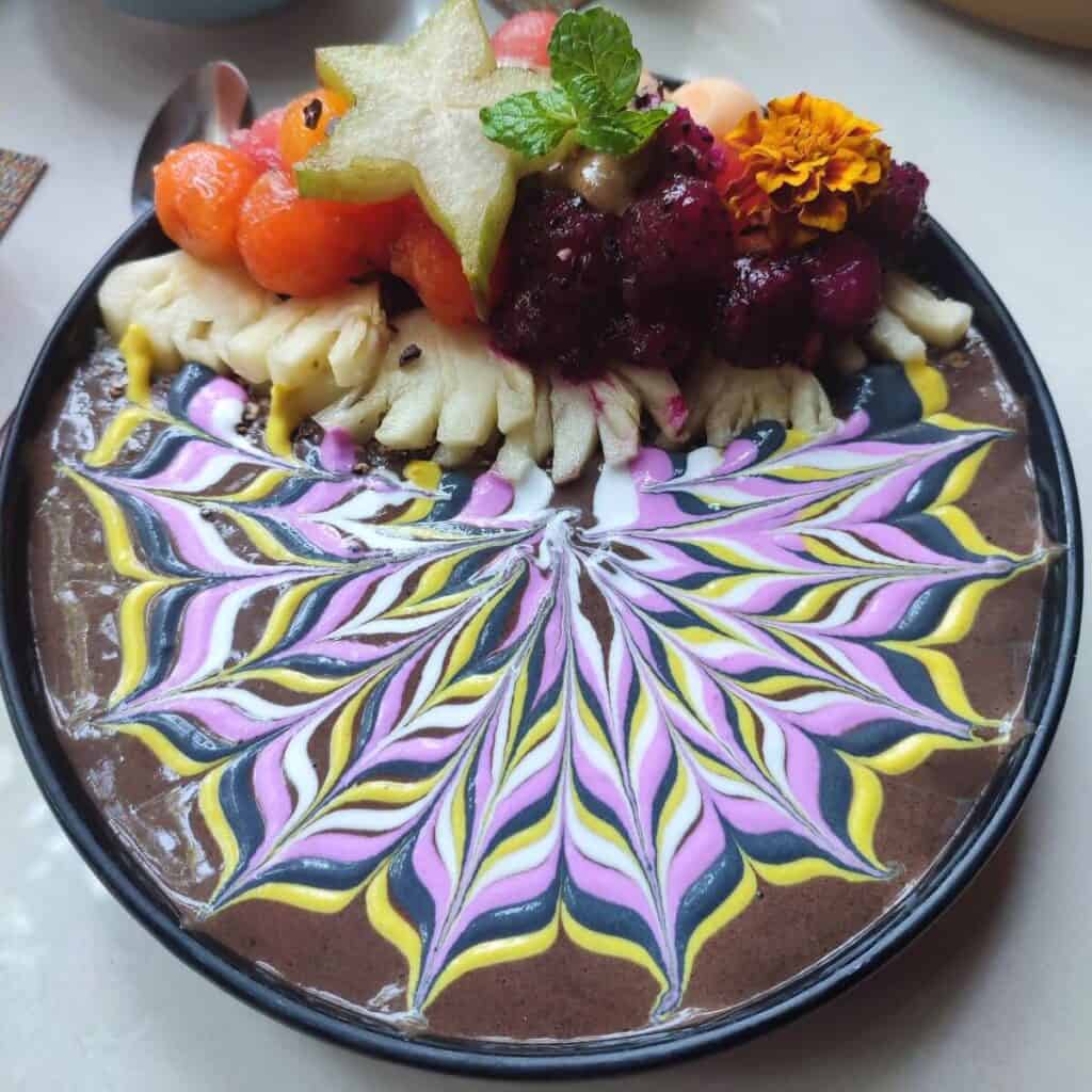 Chocolate smoothie bowl piled with fruit. The top of the yoghurt has been decorated in a colourful mandala style pattern (from Blend Cafe in Ubud, Bali).
