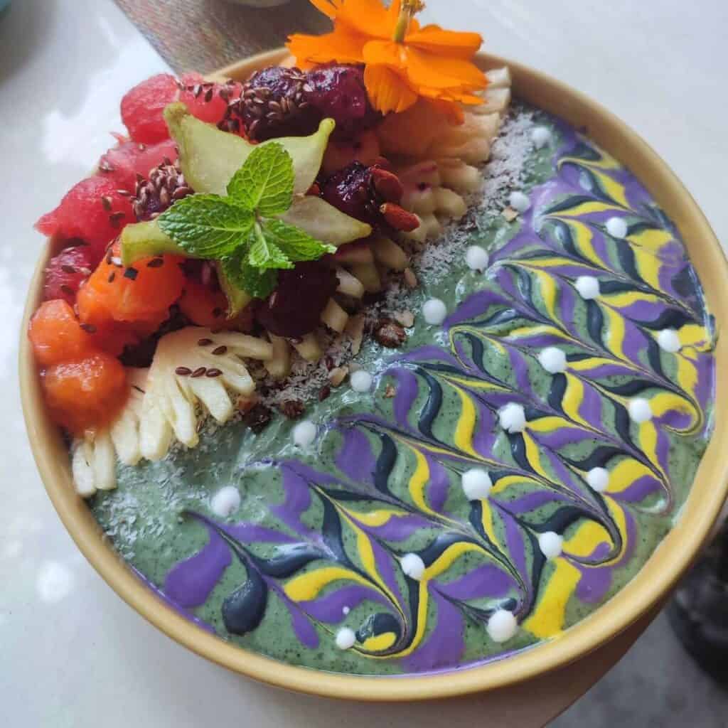 Mint spirulina smoothie bowl piled with fruit. The top of the yoghurt has been decorated in a colourful mandala style pattern (from Blend Cafe in Ubud, Bali).