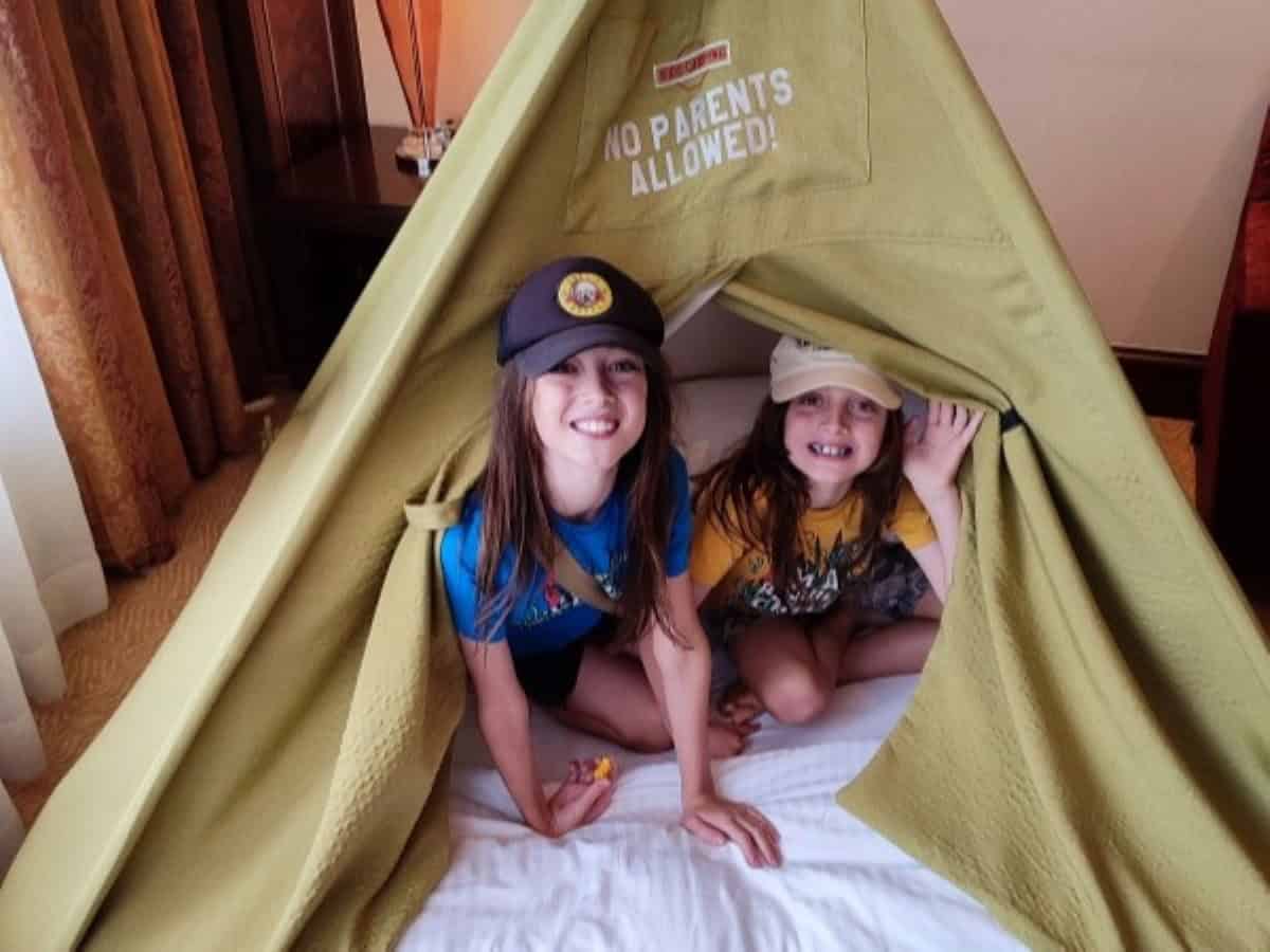 Two boys lean out from inside a khaki canvas teepee in a Family Suite at the Shangri La Kuala Lumpur. A sign stitched to the top of the teepee tent says 'No parents allowed'.