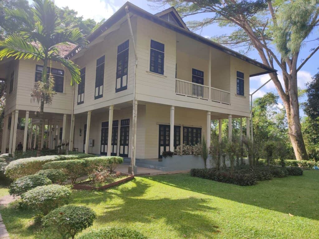 The restored Agnes Keith House in Sandakan, Borneo — a two-storey colonial-era wooden home painted cream with dark blue trim, a wraparound veranda, and a well-kept tropical garden, now a museum and one of the top historical things to do in Sandakan.
